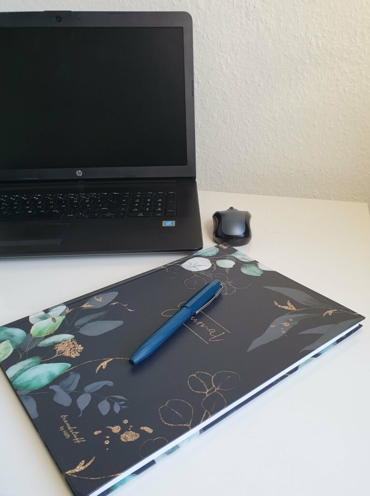 Laptop auf Schreibtisch mit Notizblock und Kulli im Vordergrund